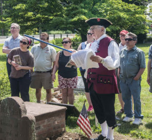 a man in breeches, vest and tricorn hat leans a tour in an old cemetery 