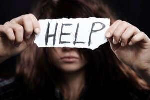 Teen holds up piece of paper with word "HELP'' written on it