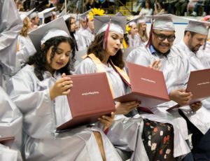 Graduates in cap and gown look at their diplomas