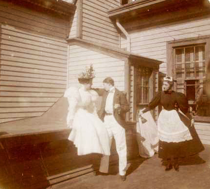 historic photo of a couple dressed in white, plus a servant nearby.