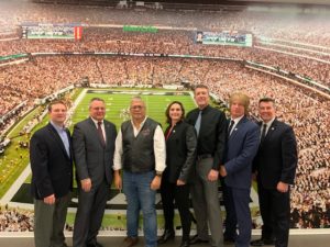 Officials pose in front of a backdrop that looks like a football stadium.